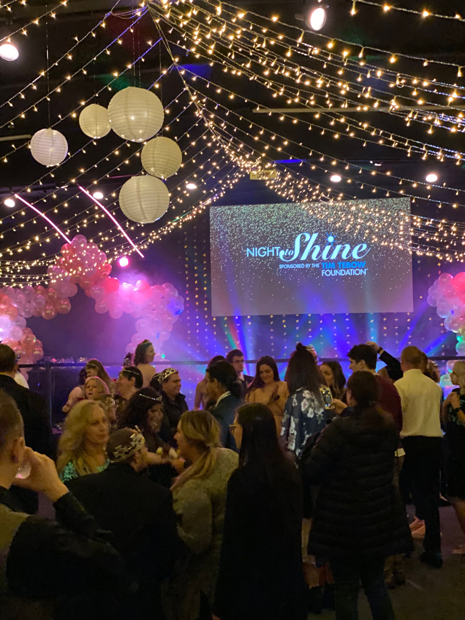 Public Event with people dancing, string lights, and a stage with a