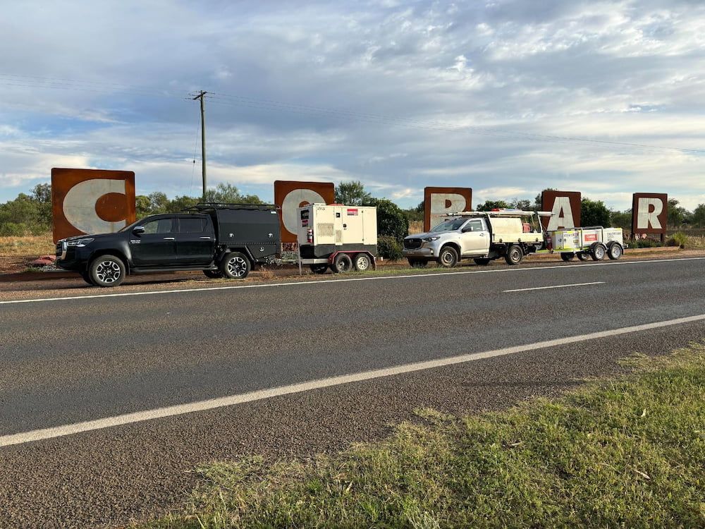 Cars and Trailers Parked at the Cobar Sign on a Road, With Cloudy Sky — Pure Plumbing & Electrical in Dubbo, NSW