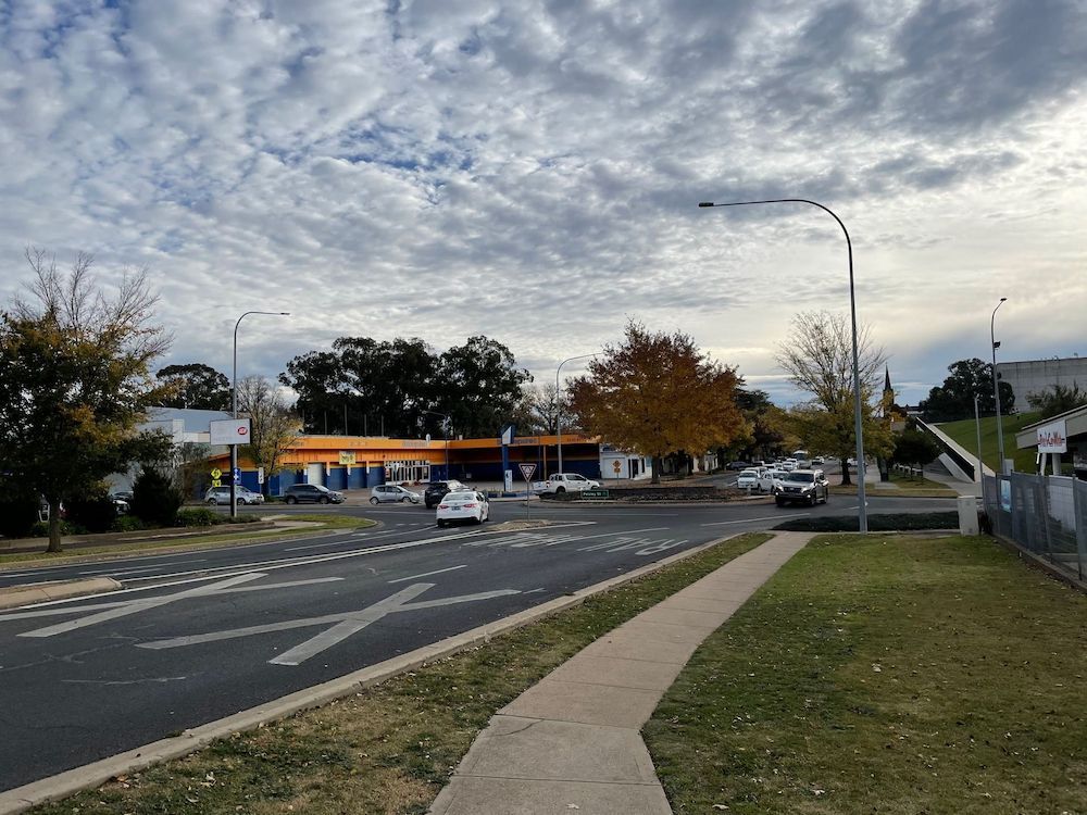 Road Intersection With Cars, Trees, Buildings, and Cloudy Sky — Pure Plumbing & Electrical in Orange, NSW