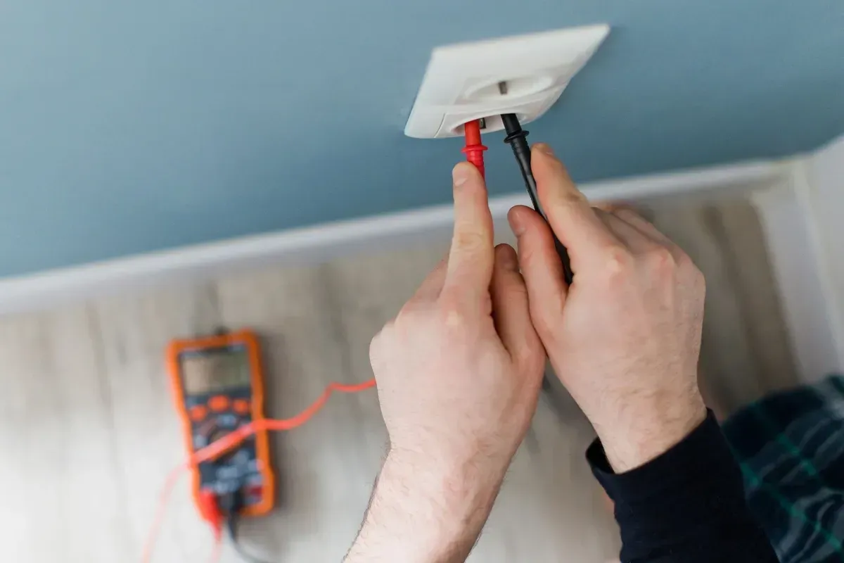 Hands Testing a Wall Outlet With a Multimeter — Pure Plumbing & Electrical in Dubbo, NSW