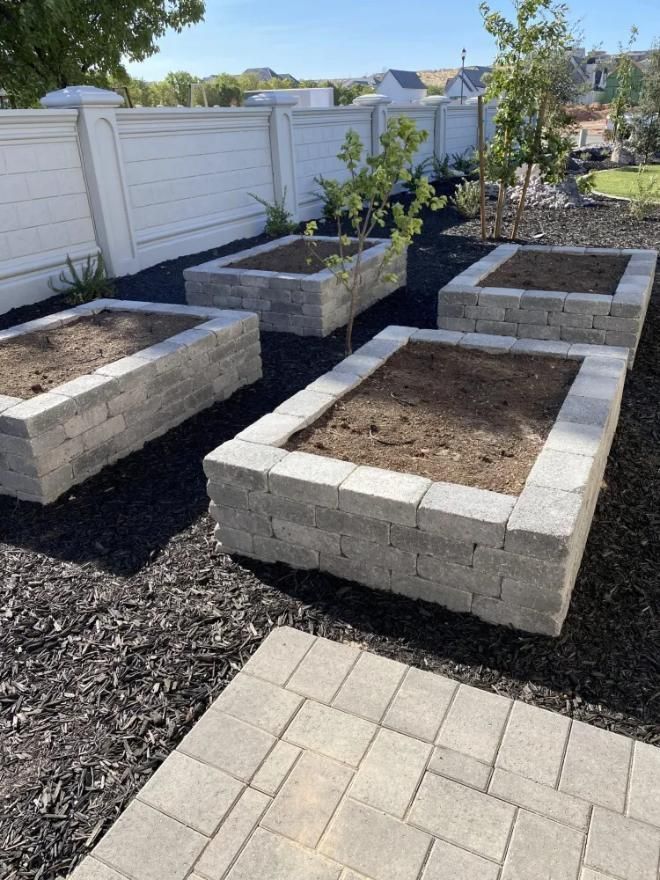 A row of concrete planters in a garden with a white fence in the background.