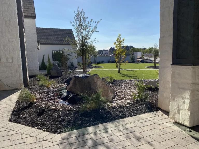 A brick walkway leading to a house with a garden in front of it.