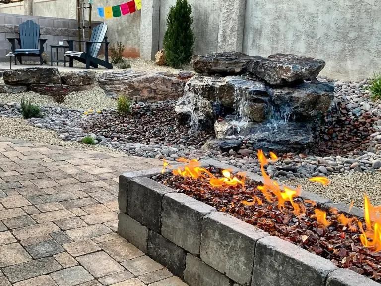 A fire pit in a backyard with a waterfall in the background.