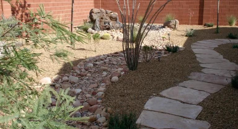 A stone walkway in a garden with a brick wall in the background.