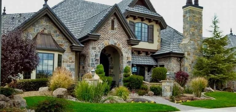 A large stone house with a gray roof and a chimney is sitting on top of a lush green lawn.