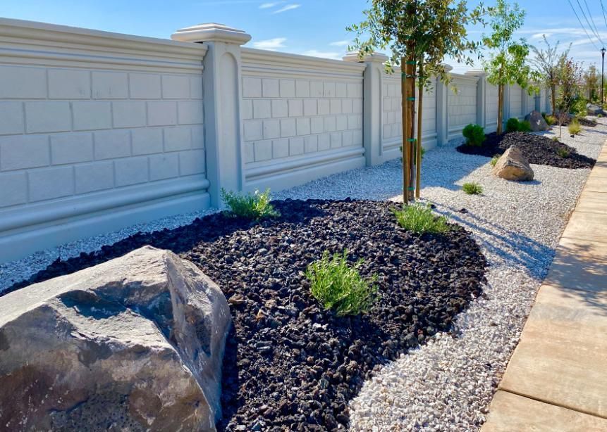 A white brick fence surrounds a garden with rocks and plants.