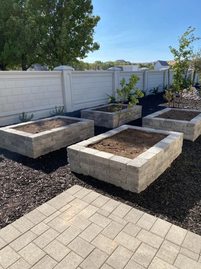 A row of concrete planters in a backyard with a white fence in the background