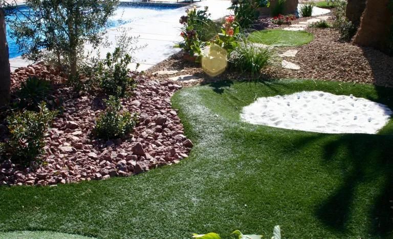 A golf course in a backyard with a pool in the background.