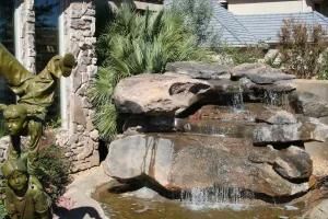 A waterfall in a garden with a statue in the background.