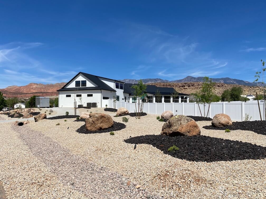 A large white house with a white fence and rocks in front of it.