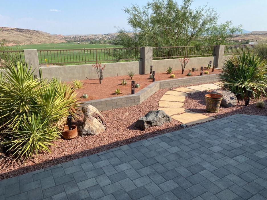 A patio with a brick walkway leading to a garden filled with plants and rocks.