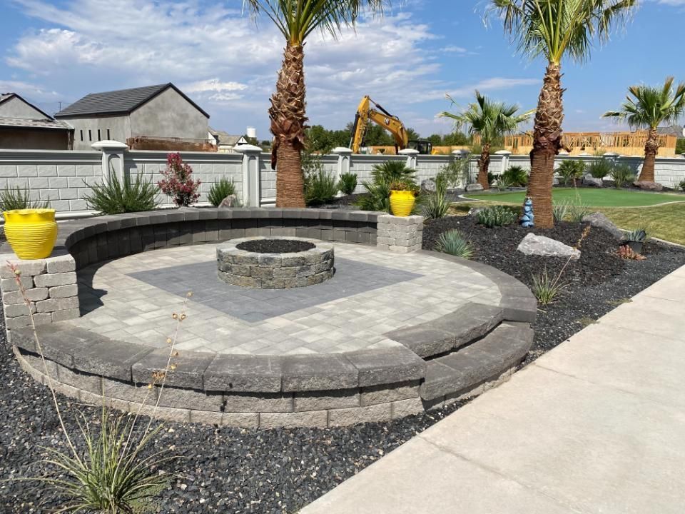 There is a fire pit in the middle of the yard surrounded by palm trees.