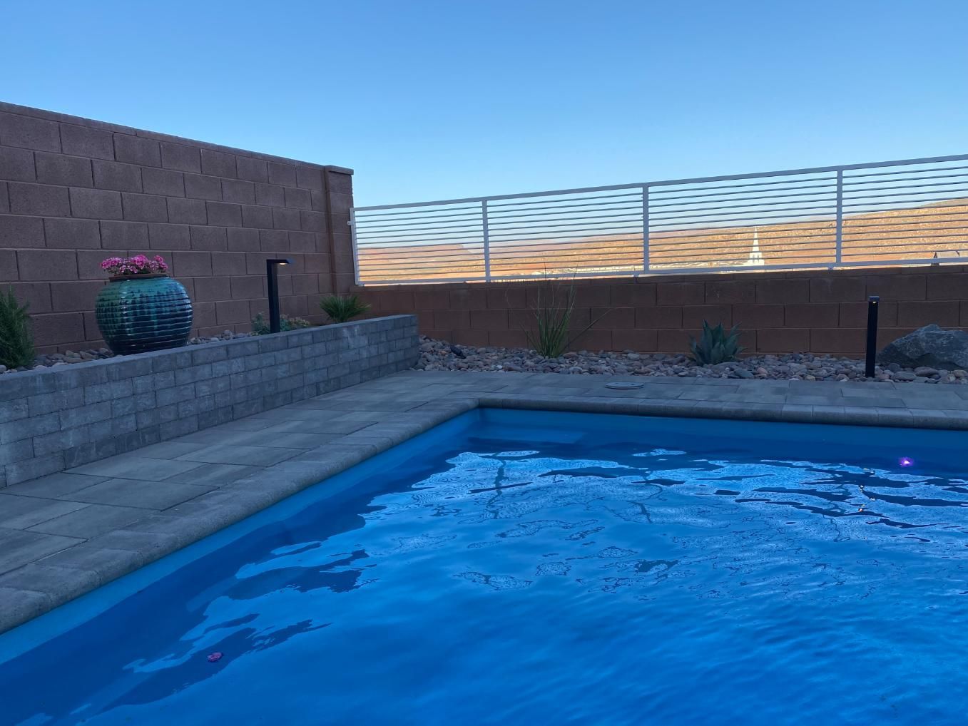 A large swimming pool is surrounded by a brick wall and a fence.