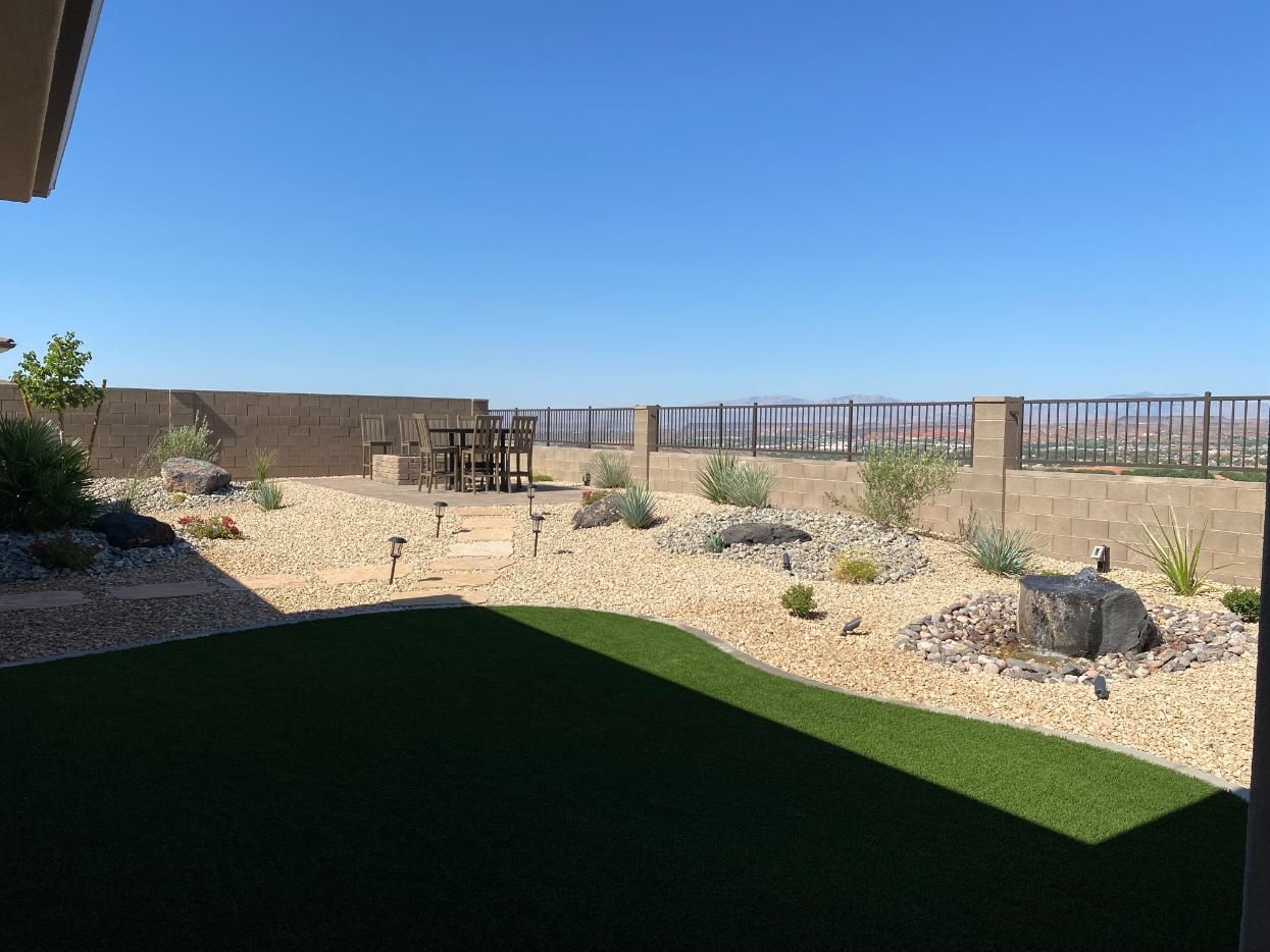 A backyard with a lot of grass and rocks and a fence.