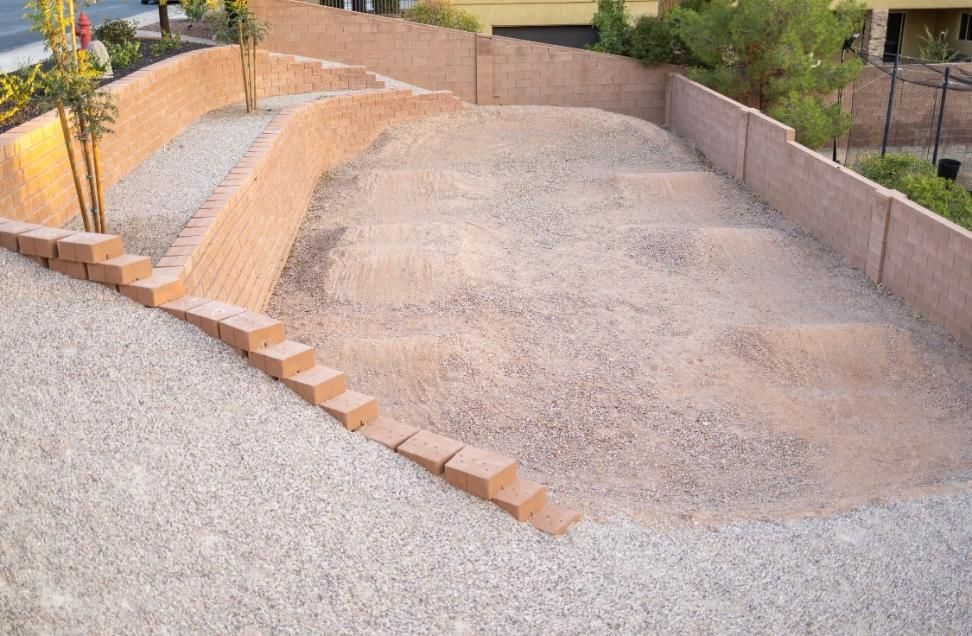 A brick wall surrounds a gravel area with stairs leading up to it.