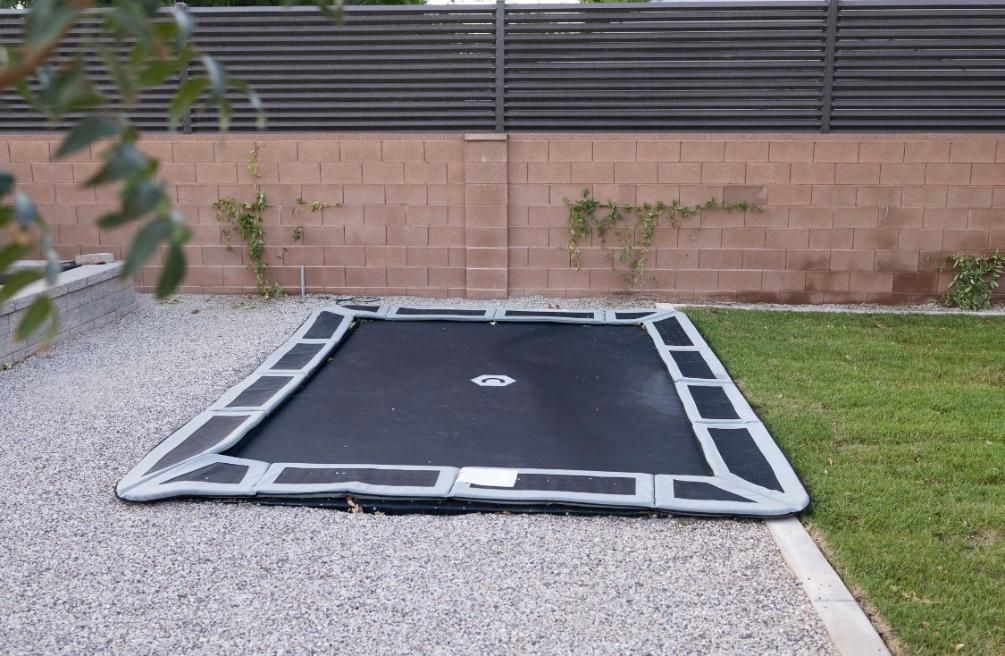 A trampoline is sitting in the grass in front of a brick wall