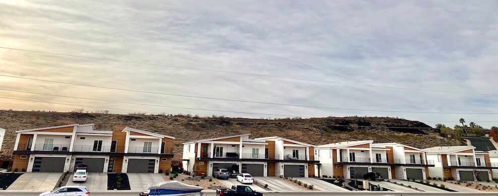 A row of houses on a hill with cars parked in front of them.