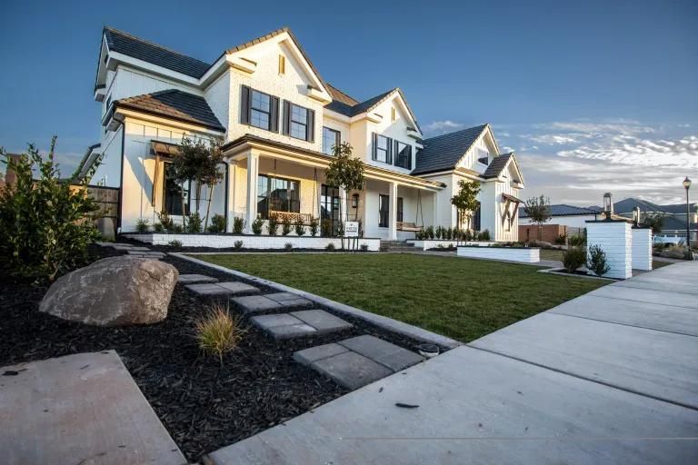 A large white house with black shutters is sitting on top of a lush green lawn.