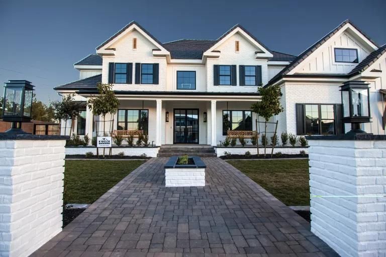 A large white house with black shutters and a brick walkway