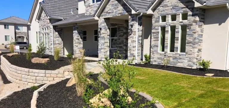 A large house with a lush green lawn and a stone wall in front of it.