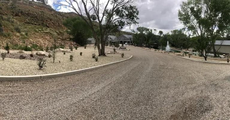 A gravel road leading to a house with trees on the side of it.