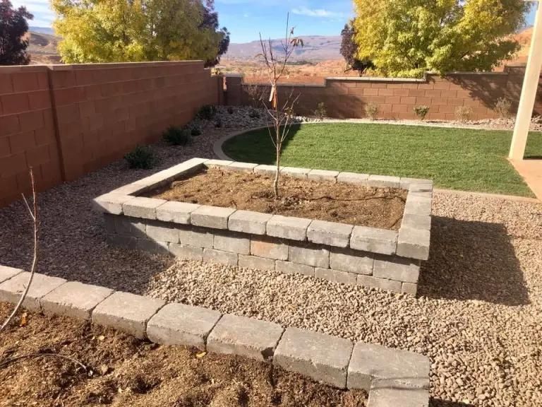 A brick planter with a tree in it in a backyard.