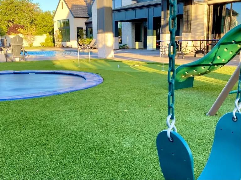 A swing set in a backyard with a slide and a trampoline.