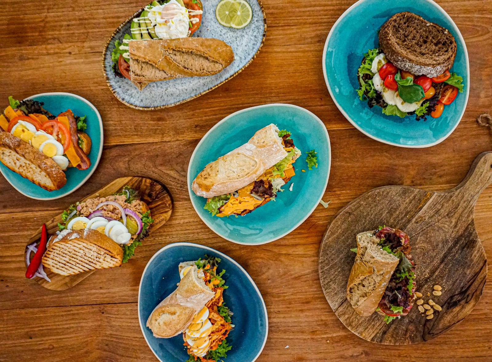 Een assortiment sandwiches op verschillende borden en houten planken op een houten tafel.