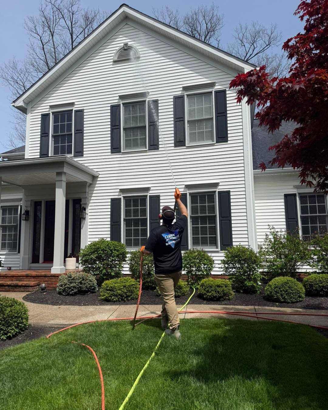 Person spraying a white house lawn with a hose in a sunny front yard