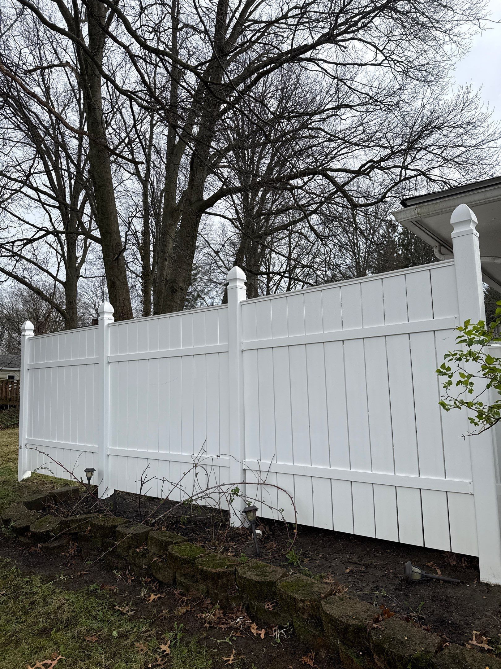White vinyl fence along a wooded hillside under cloudy sky