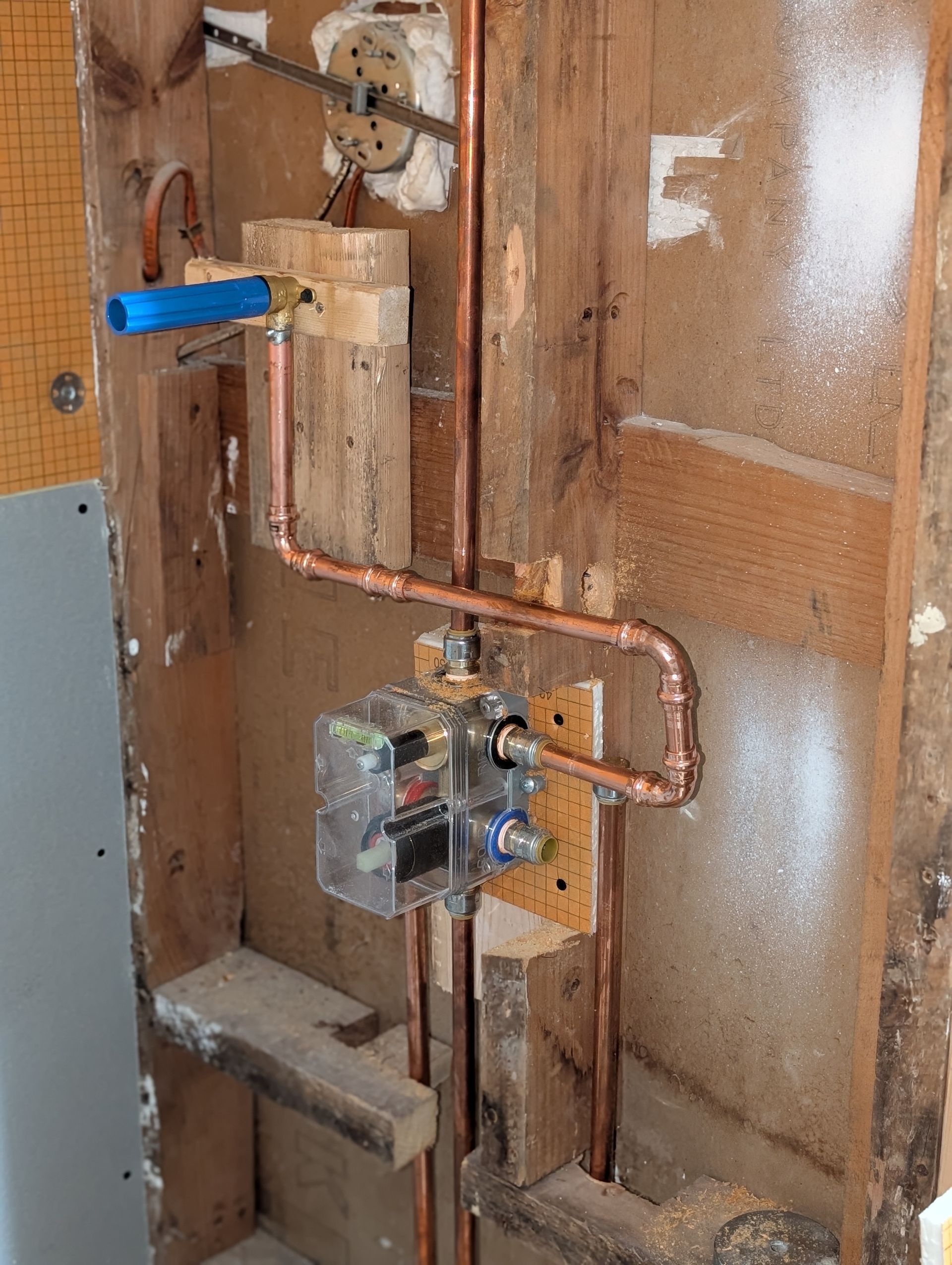 Copper plumbing pipes and shower valve installed inside a wooden wall frame during renovation.