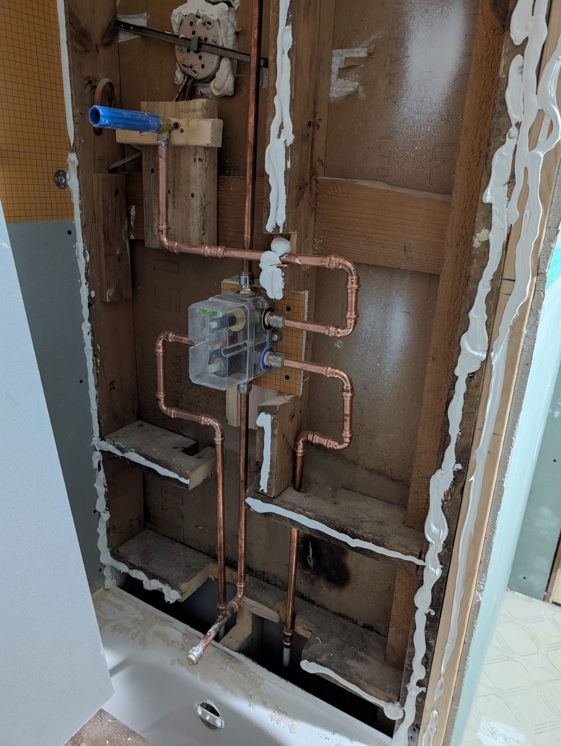 Copper pipes and shower valve installed in a wall opening; wooden studs and shelves are visible.
