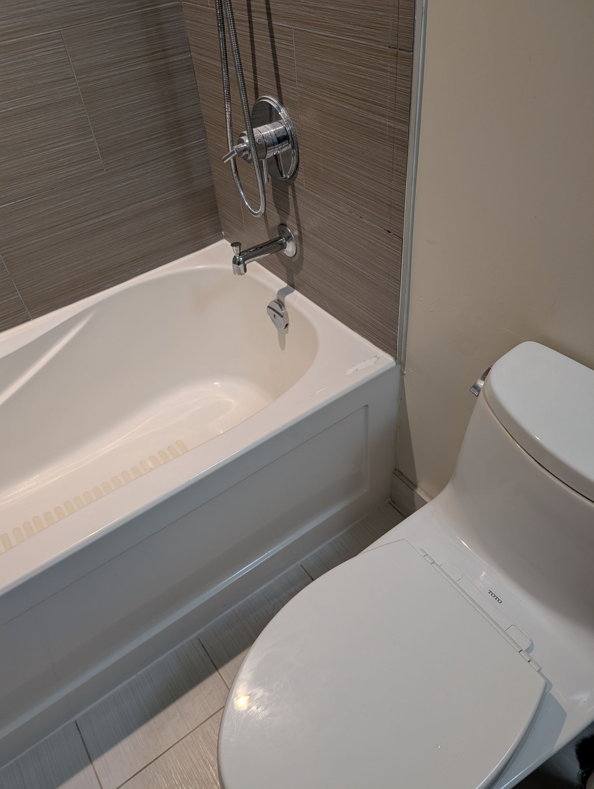 A white bathtub and toilet are next to each other in a bathroom with textured tan tile.