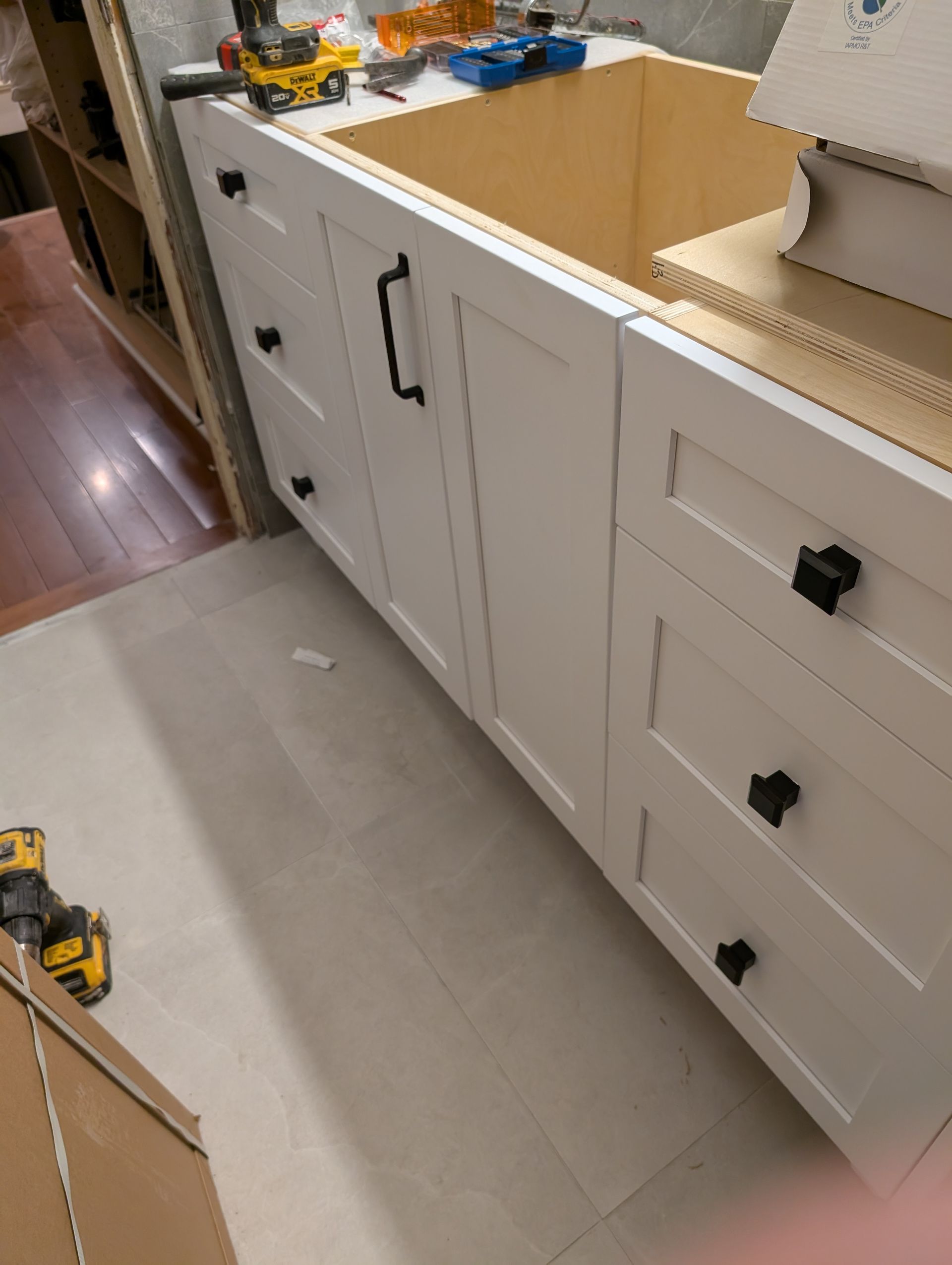 White bathroom vanity with black hardware installed against a wall. A drill and tools are visible.