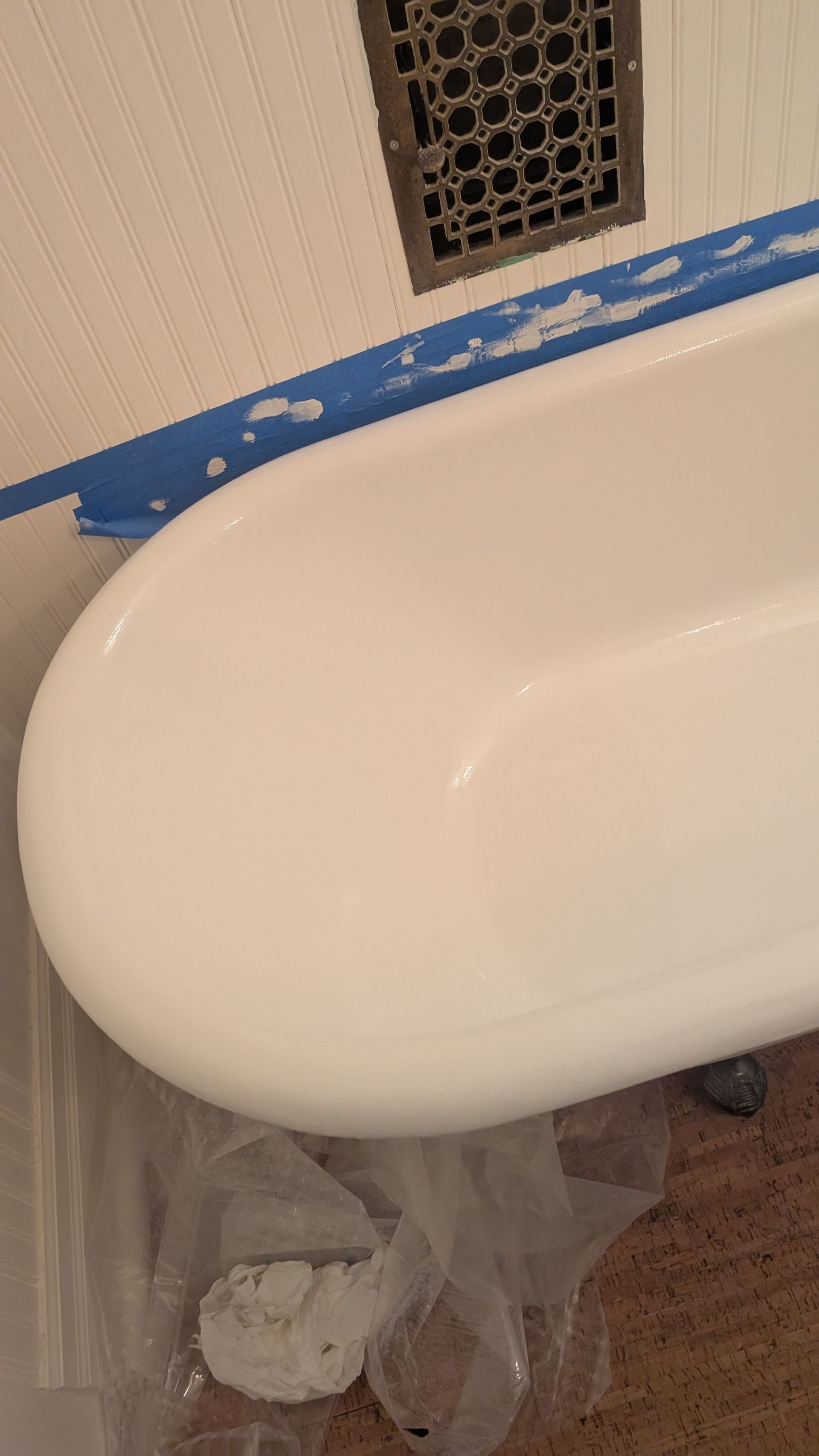 White bathtub in bathroom, blue tape along wall, ventilation vent visible.