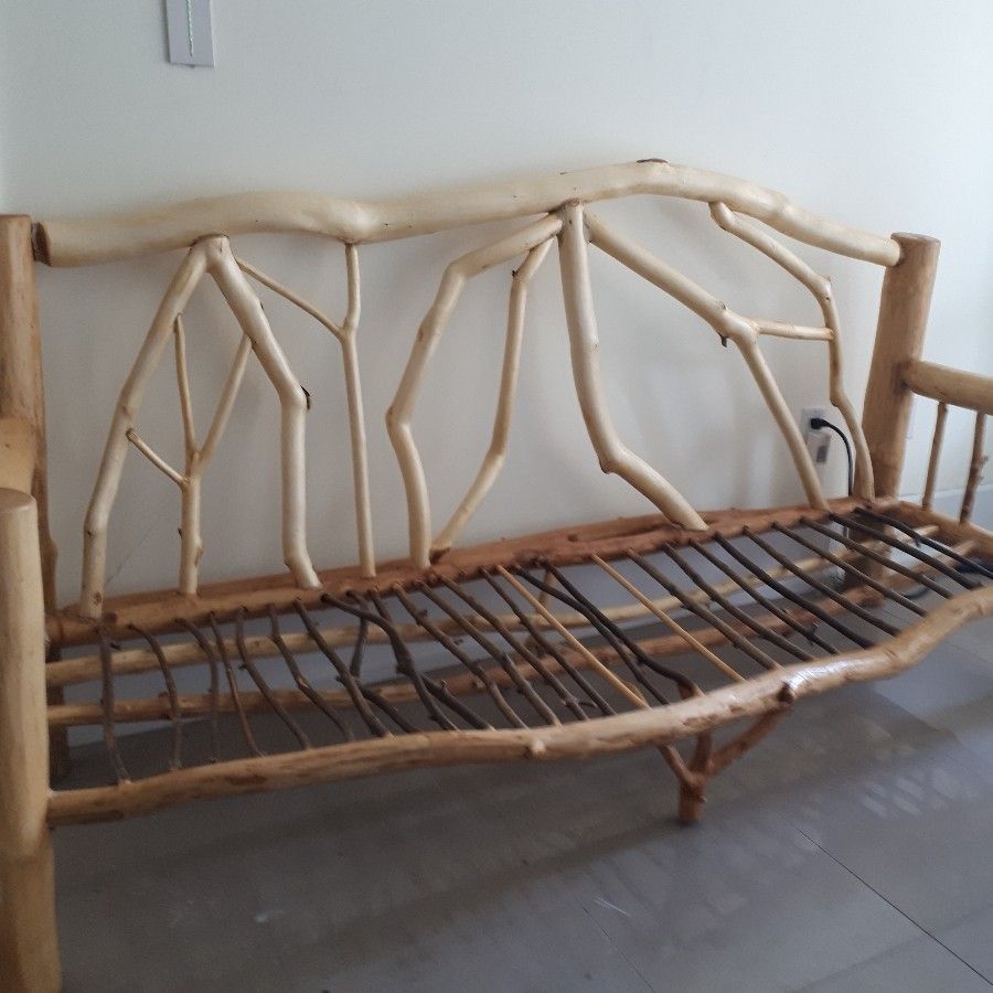 Rustic wooden bench with branch-like back and arm supports, metal wire seat, indoors.
