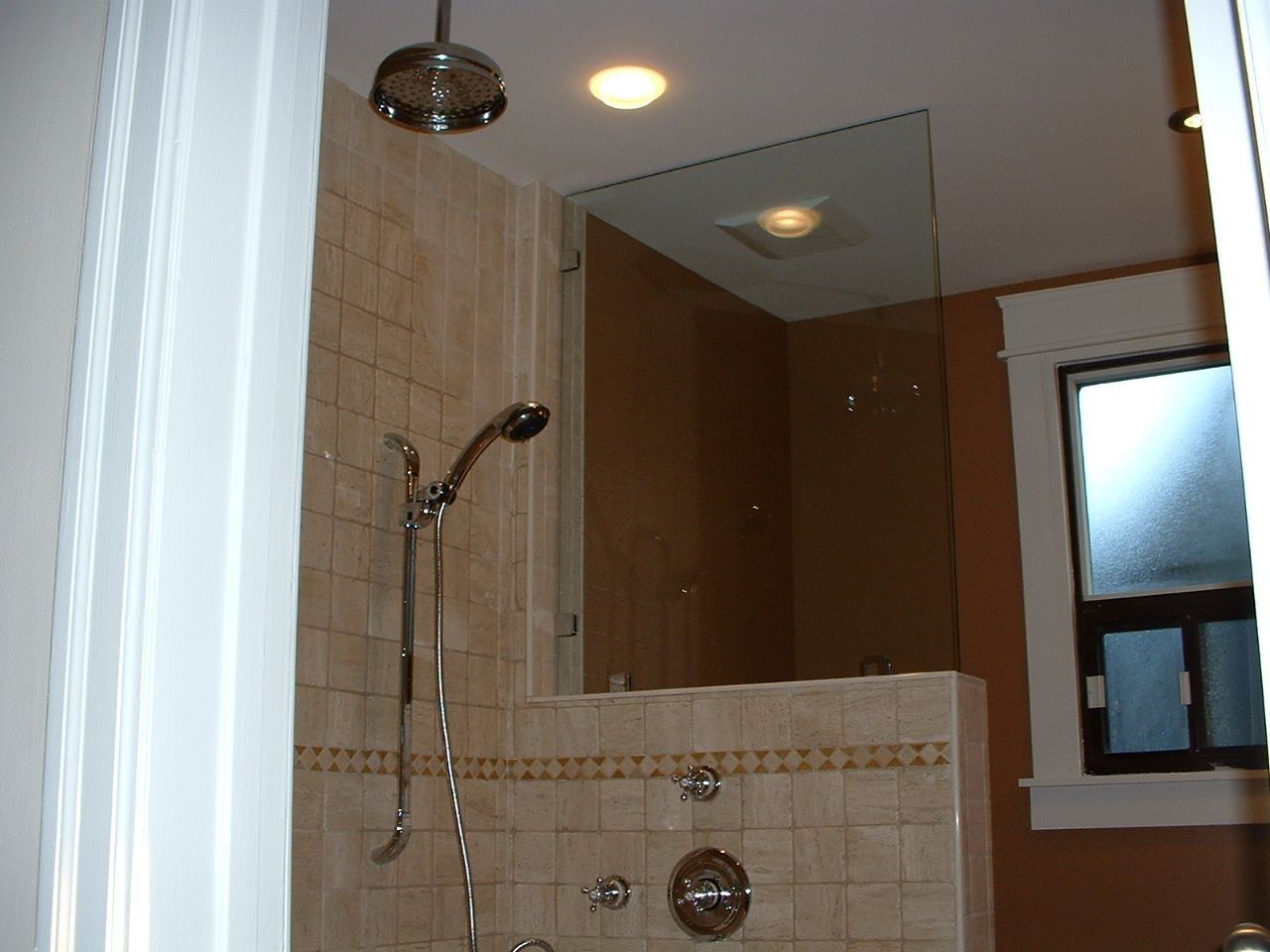 Bathroom shower stall with beige tile, glass door, and chrome fixtures.