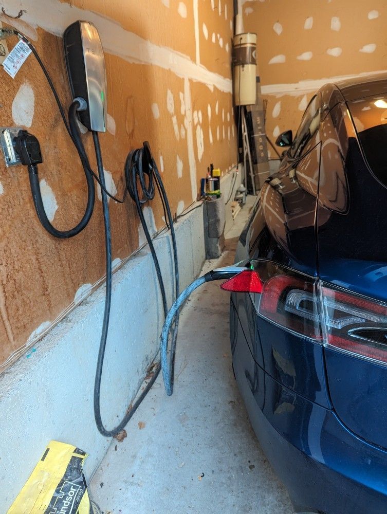 Blue Tesla charging in a garage with a charger attached. The walls are unfinished.