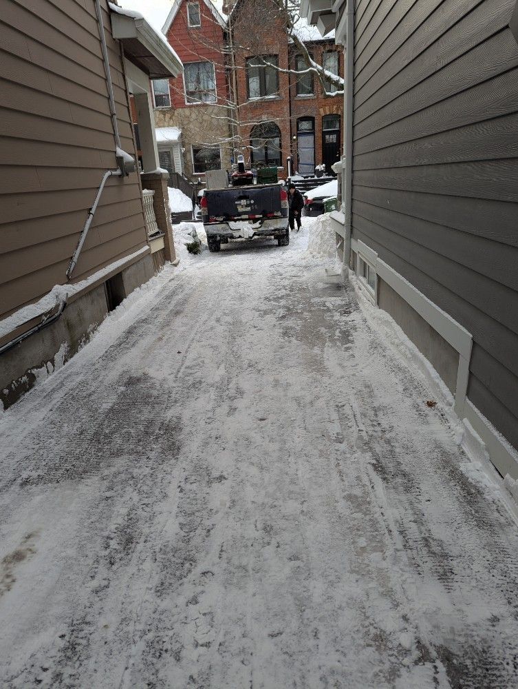 A snowy alley between two buildings, with a truck parked in the distance.