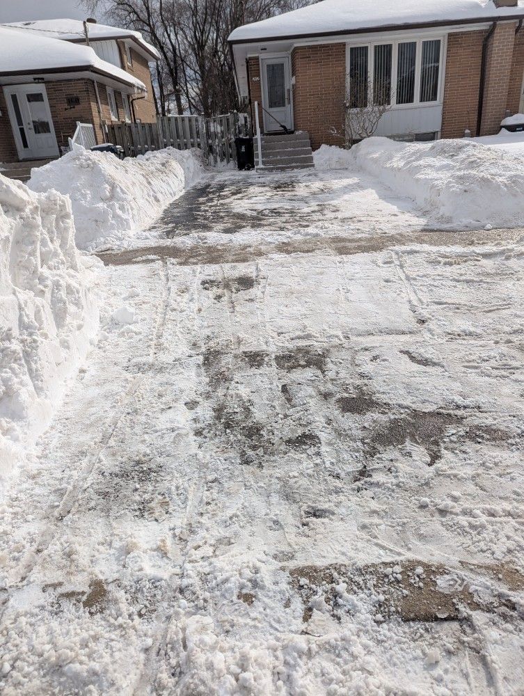 Snow-covered driveway and sidewalk leading to a brick house with a cleared path.