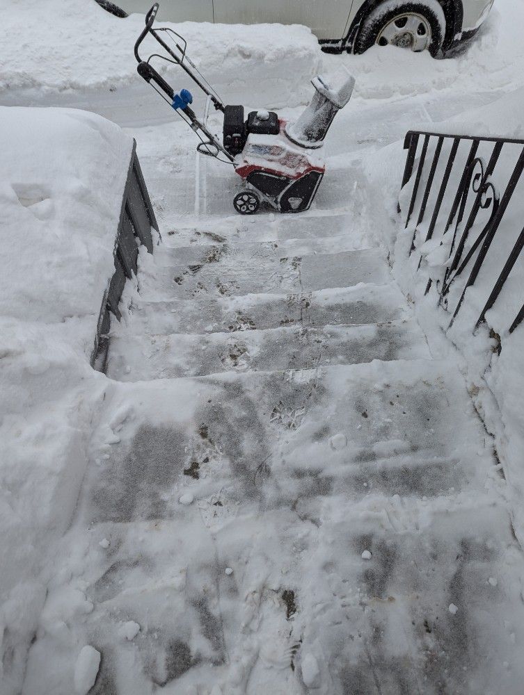Snowblower clearing snow from outdoor steps.