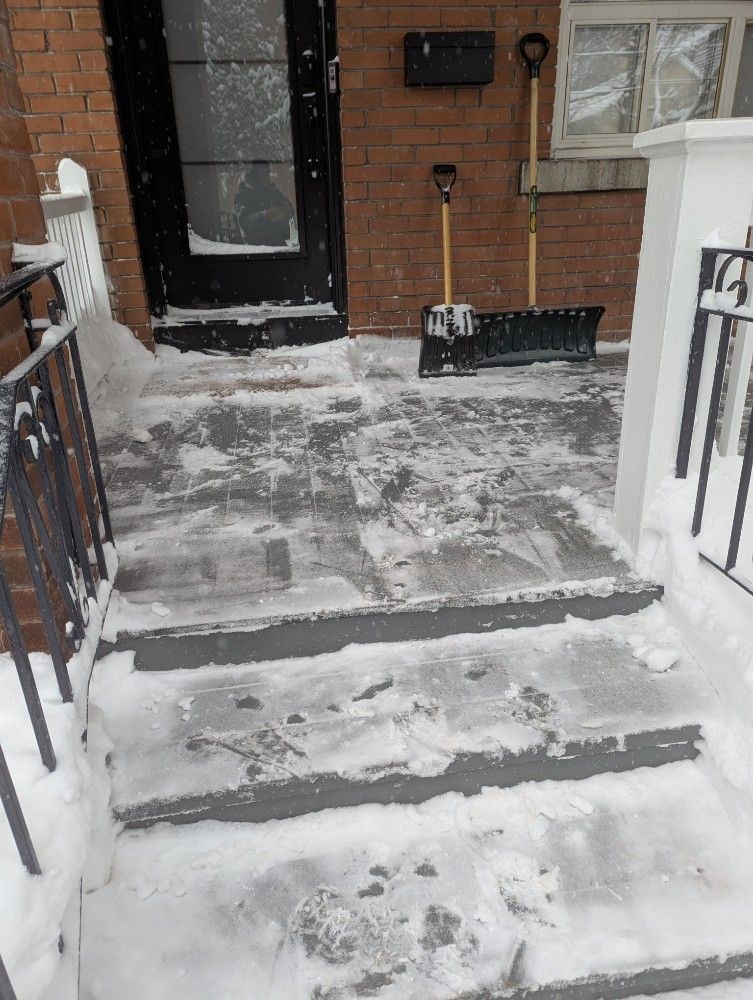 Snow-covered steps and porch leading to a black door. Snow shovels stand nearby.