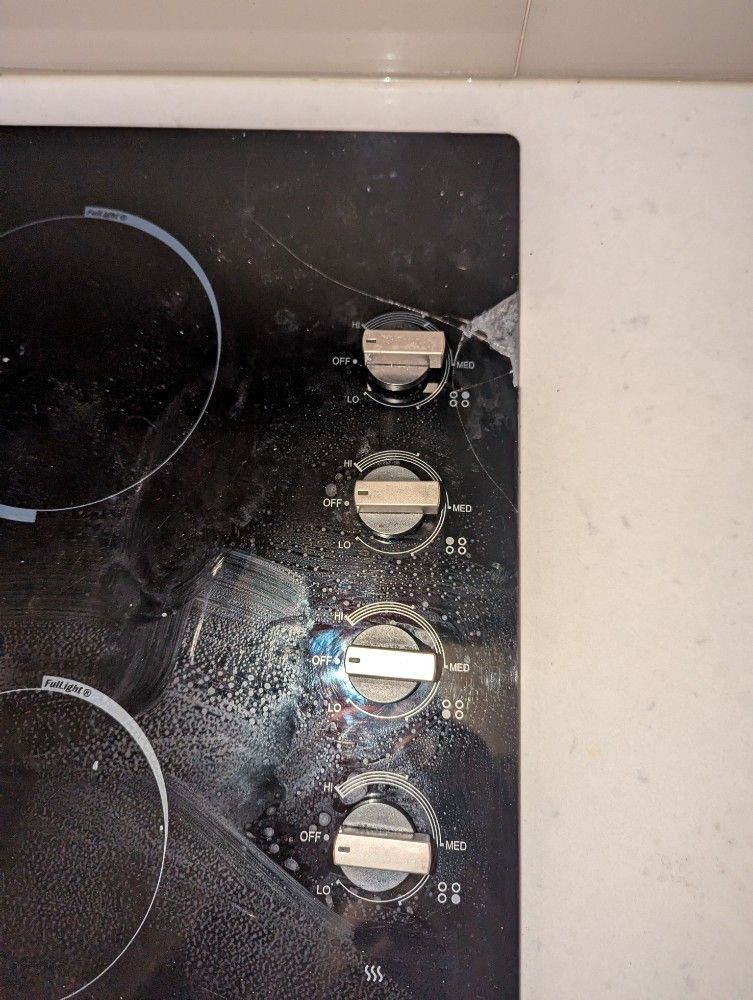 Black electric stovetop with control knobs, showing use and wear.