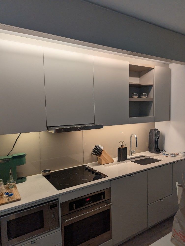 Modern kitchen with light gray cabinets, countertop, and appliances. Overhead lighting illuminates the space.