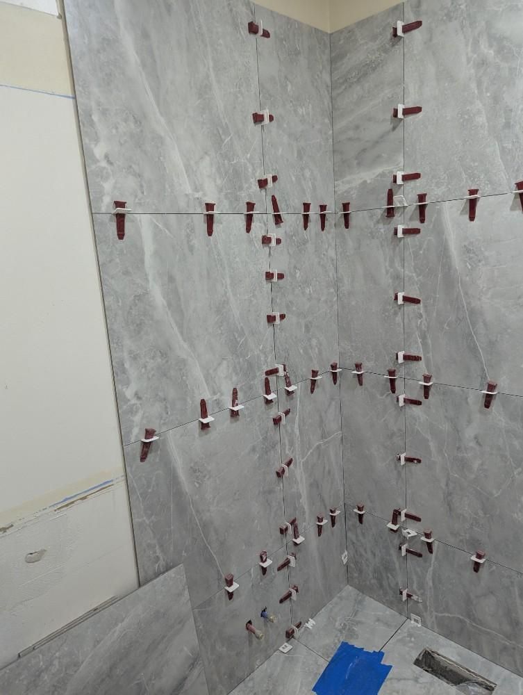 Gray tiled bathroom wall, with tile leveling clips, in progress.