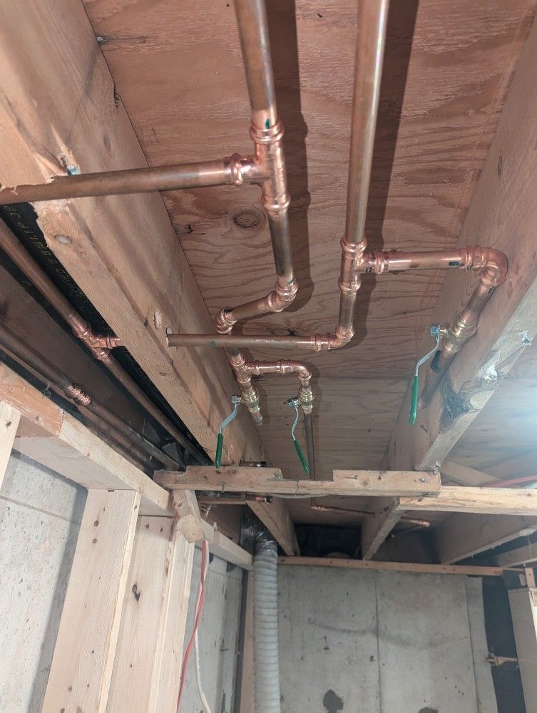 Copper pipes installed in a wooden ceiling, with valves, in a basement setting.
