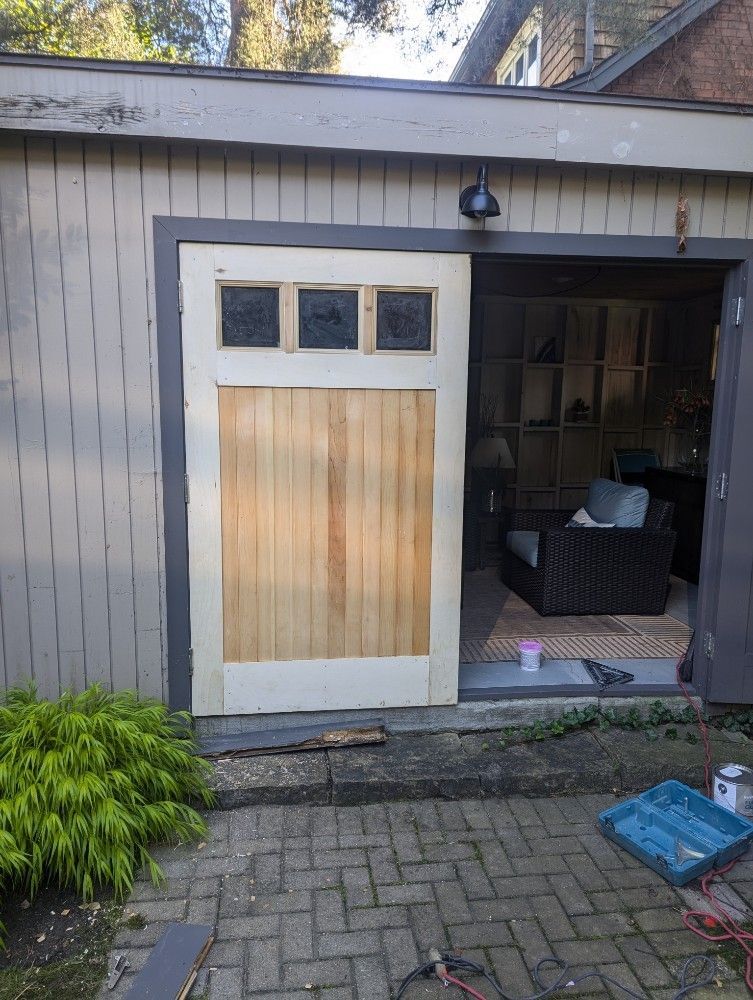 A wooden door with glass panels is open to a patio. A house and a green bush are in the background.