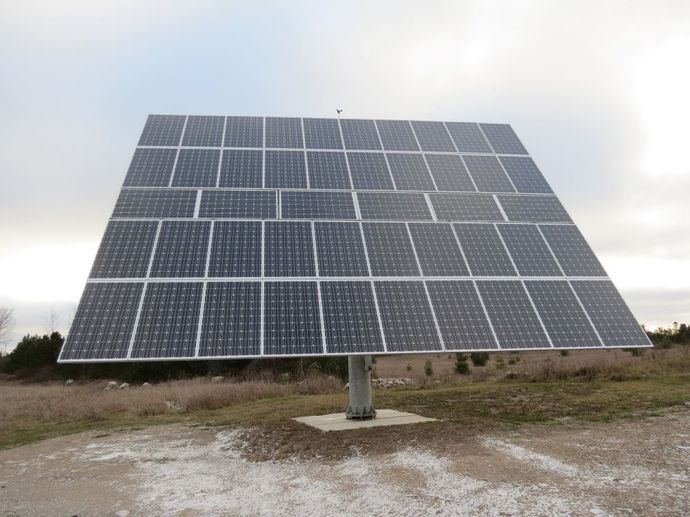 Solar panel array in a field, angled to catch sunlight on a cloudy day.