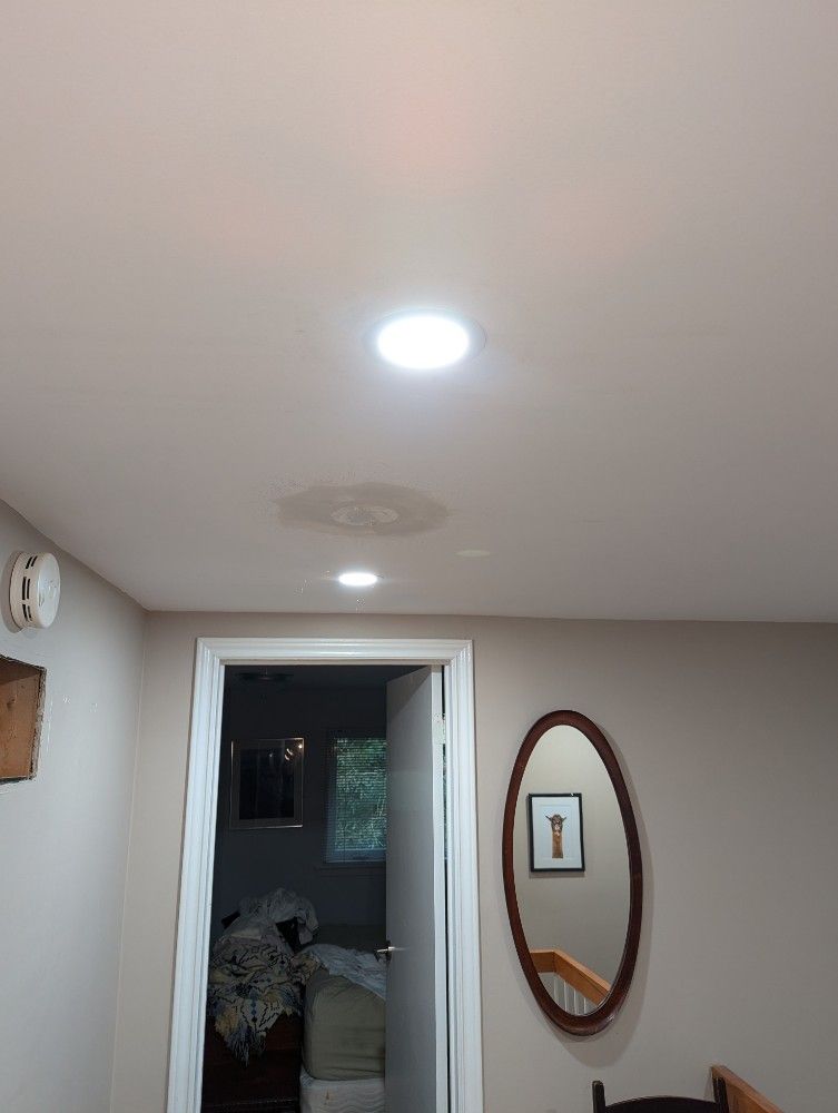 A ceiling with a water stain, two recessed lights, an open doorway, and a wall mirror.