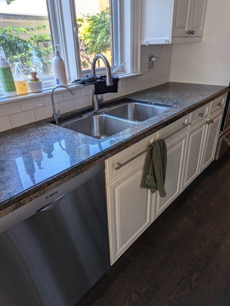 Kitchen with a stainless steel sink, granite countertop, white cabinets, and dishwasher. A green towel hangs on a cabinet.